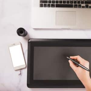 Mano che usa una tavoletta grafica accanto a laptop e smartphone, concetto di lavoro creativo digitale