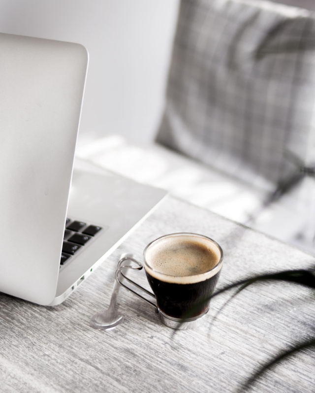 Tazza di caffè su tavolo accanto a laptop, immagine ambientata per pagina contatti Nelly Graphics